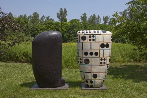 Two large ceramic sculptures, one black and one white with multi-colored lines and black dots, in a grassy area