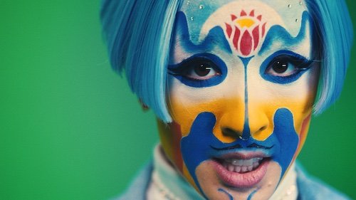 A closeup of a person in blue and yellow facepaint and a blue wig