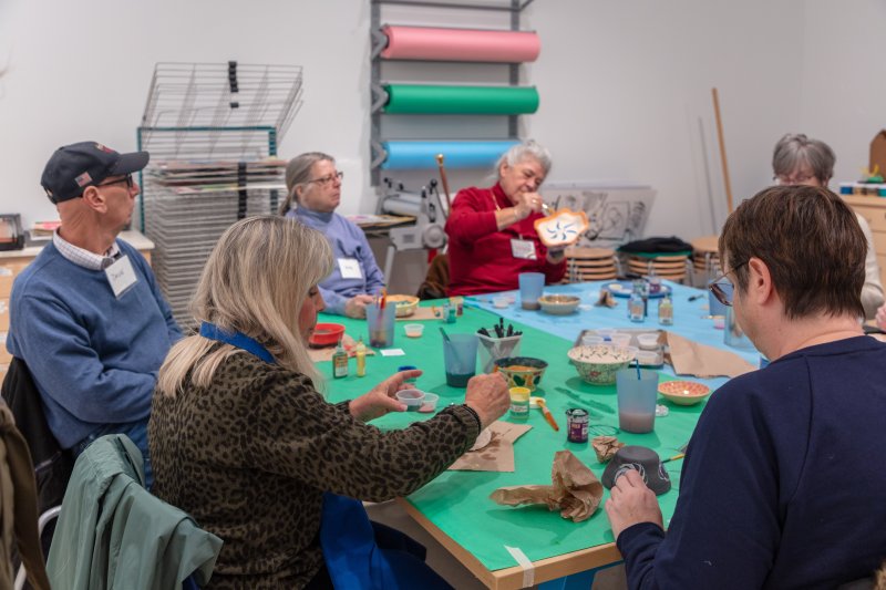 A group of elderly people painting ceramics in an art studio