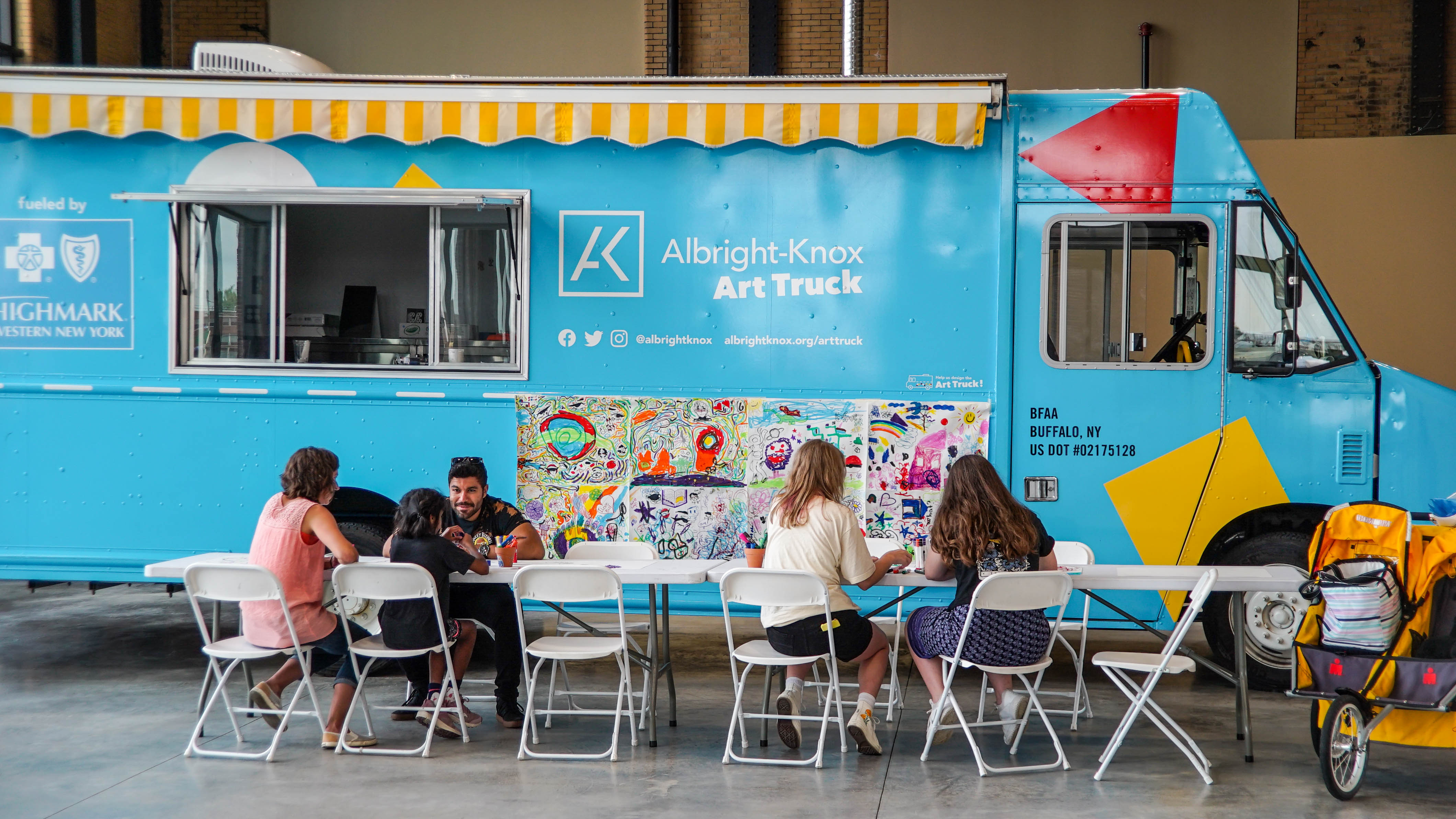 Adults and kids around a table making art in front of a large blue truck