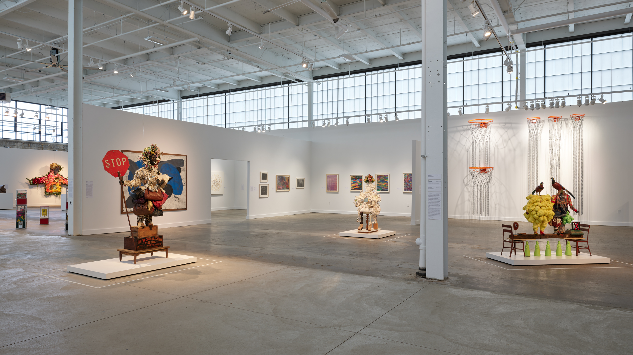 An installation view of sculptures, paintings, and installation artworks in a large industrial gallery space