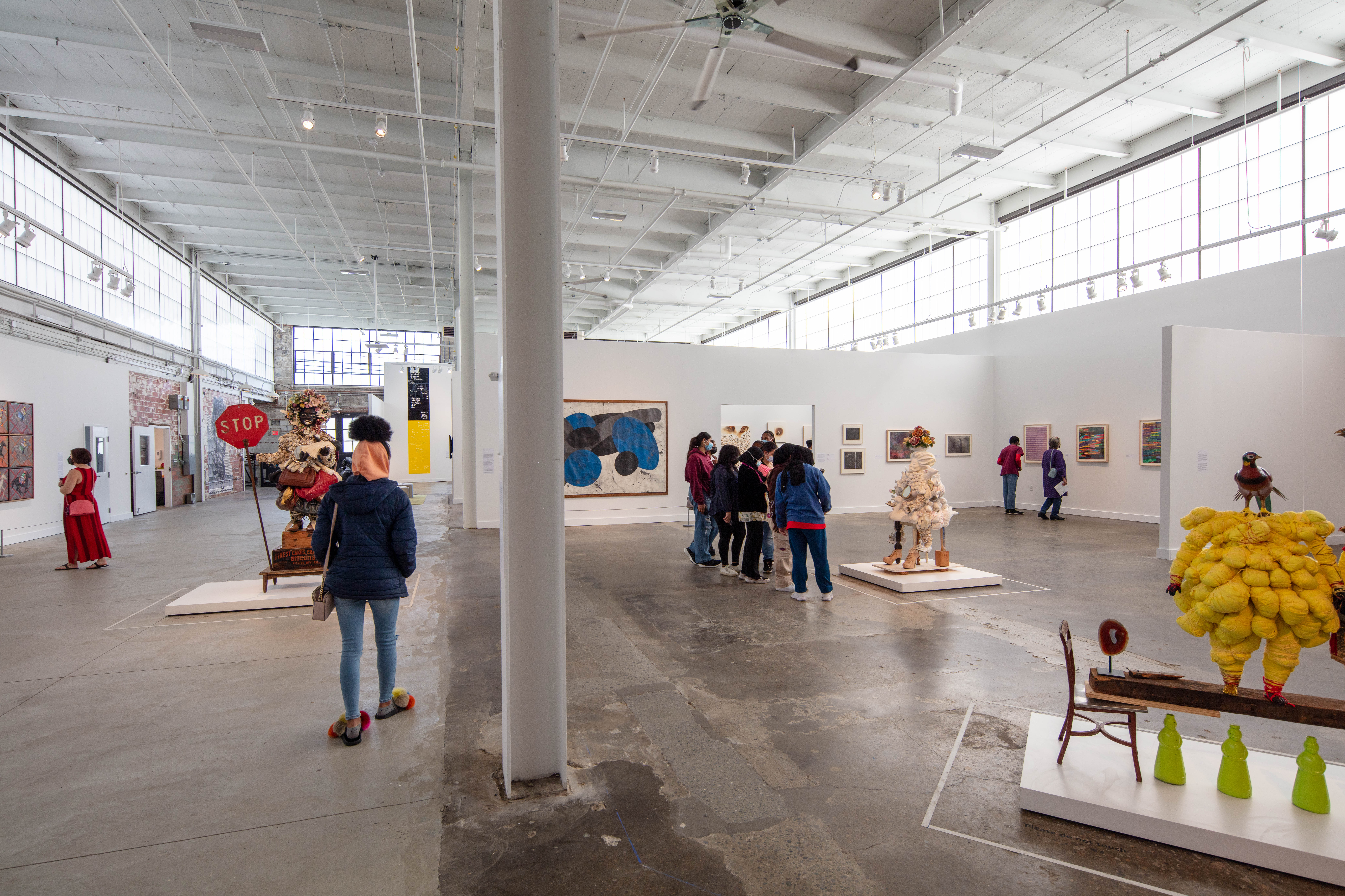 An installation view of sculptures, paintings, and installation artworks in a large industrial gallery space