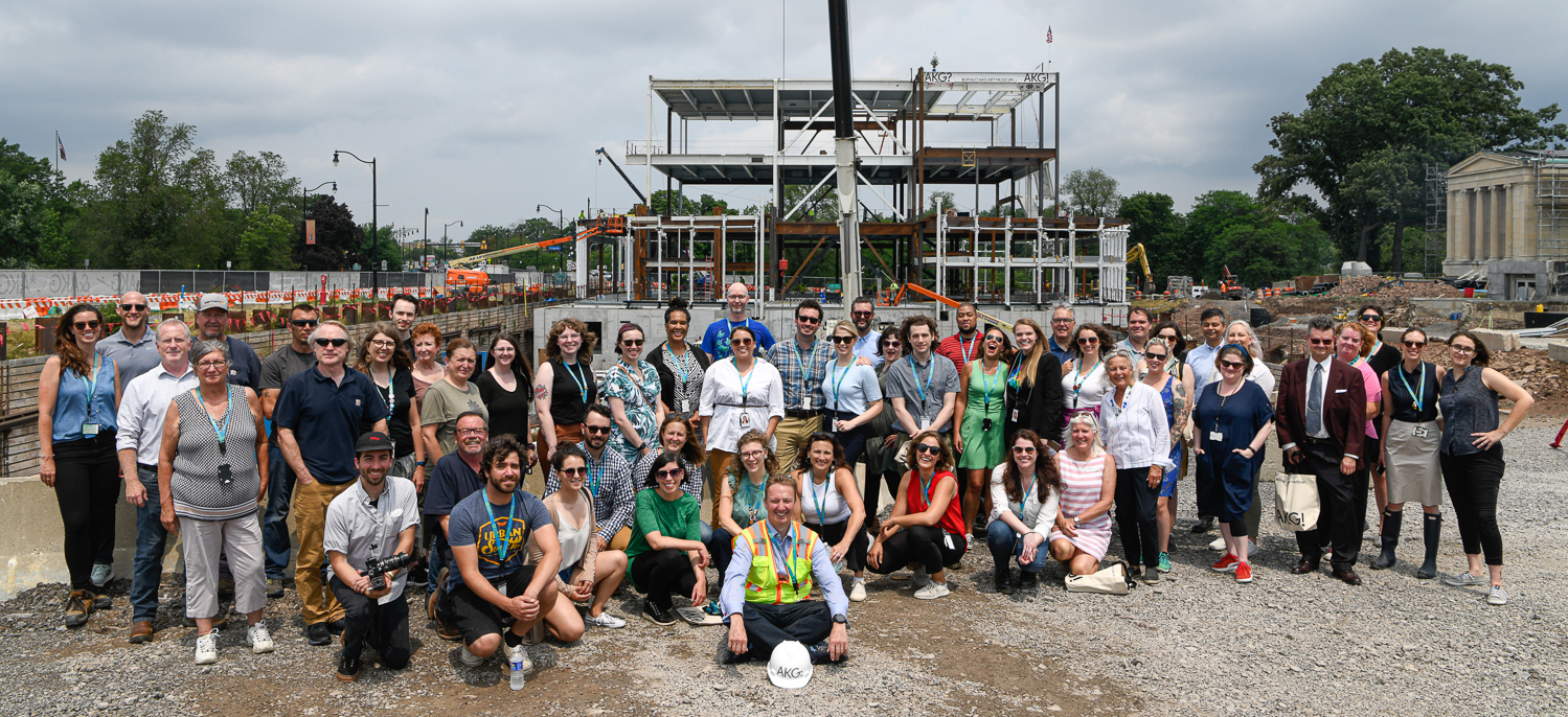 A group of people on a construction site in front of a large steel frame of a new building