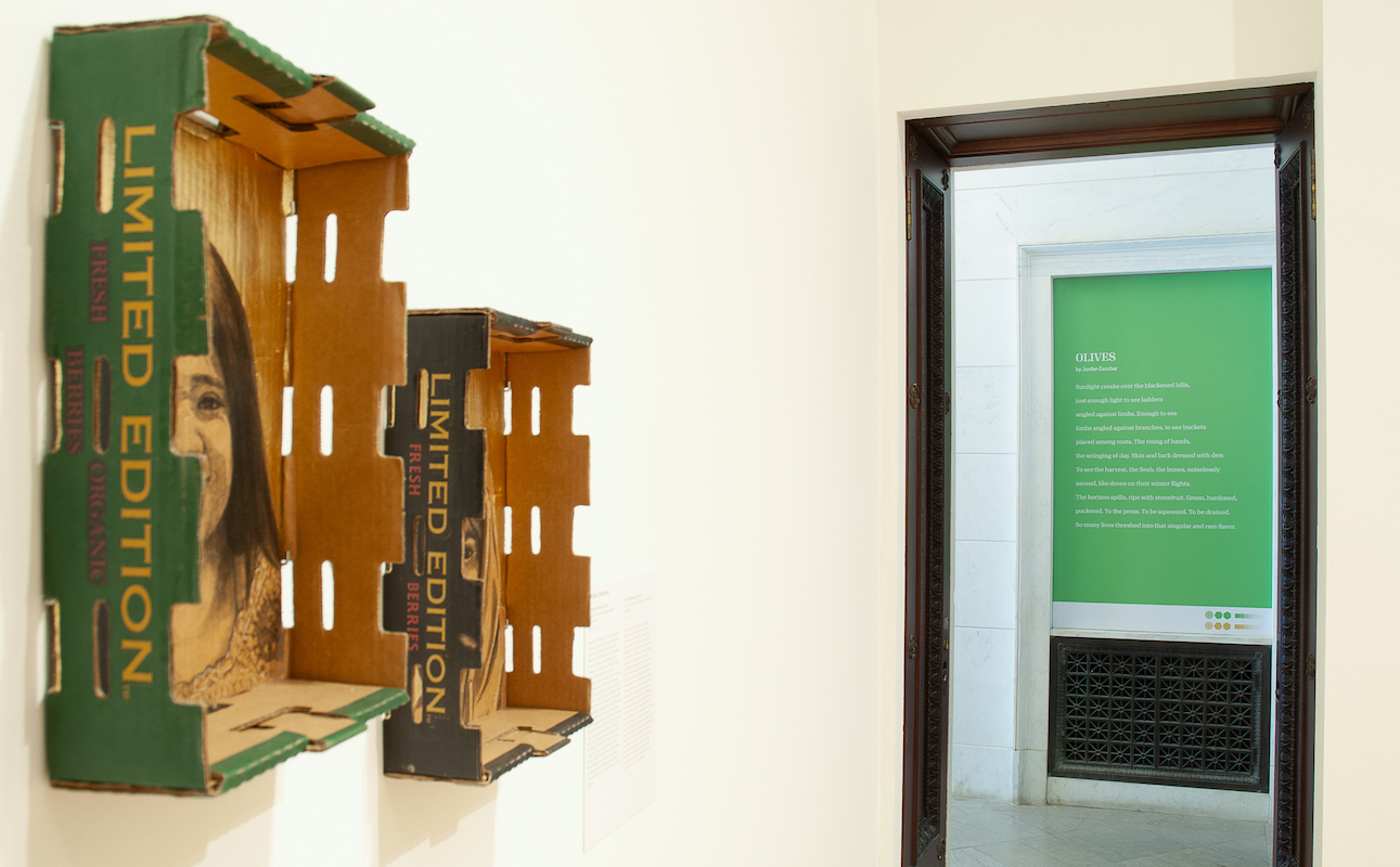 Sideway view of two artworks of portraits painted on produce boxes with a doorway displaying a large print of a poem on green paper in white font