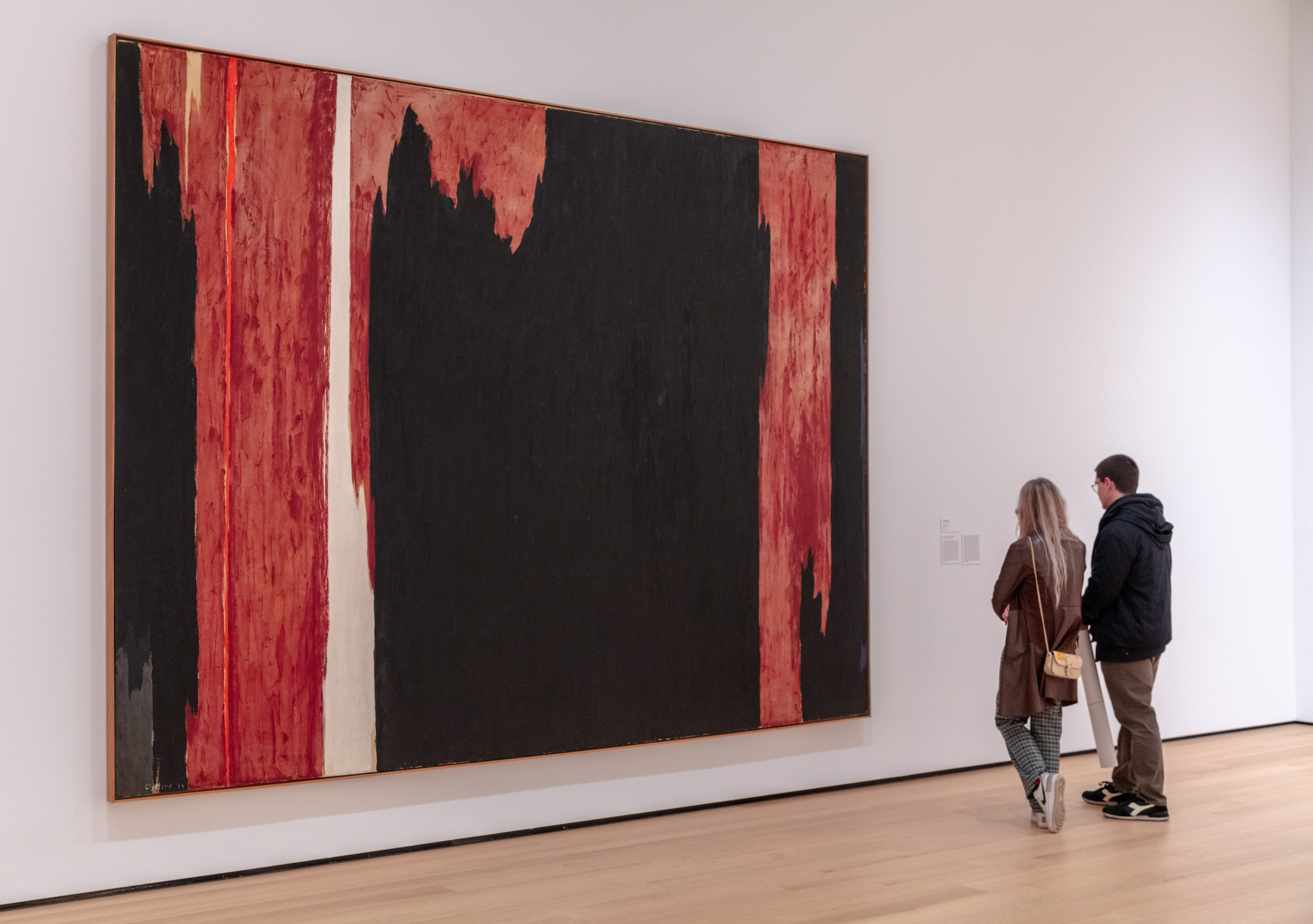 A man and woman standing in front of a large abstract painting that consists of shades of red, white, and black