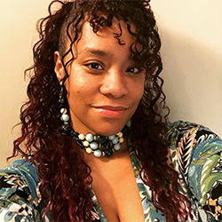 A Black woman with long curly hair wearing a colorful shirt and beaded necklace