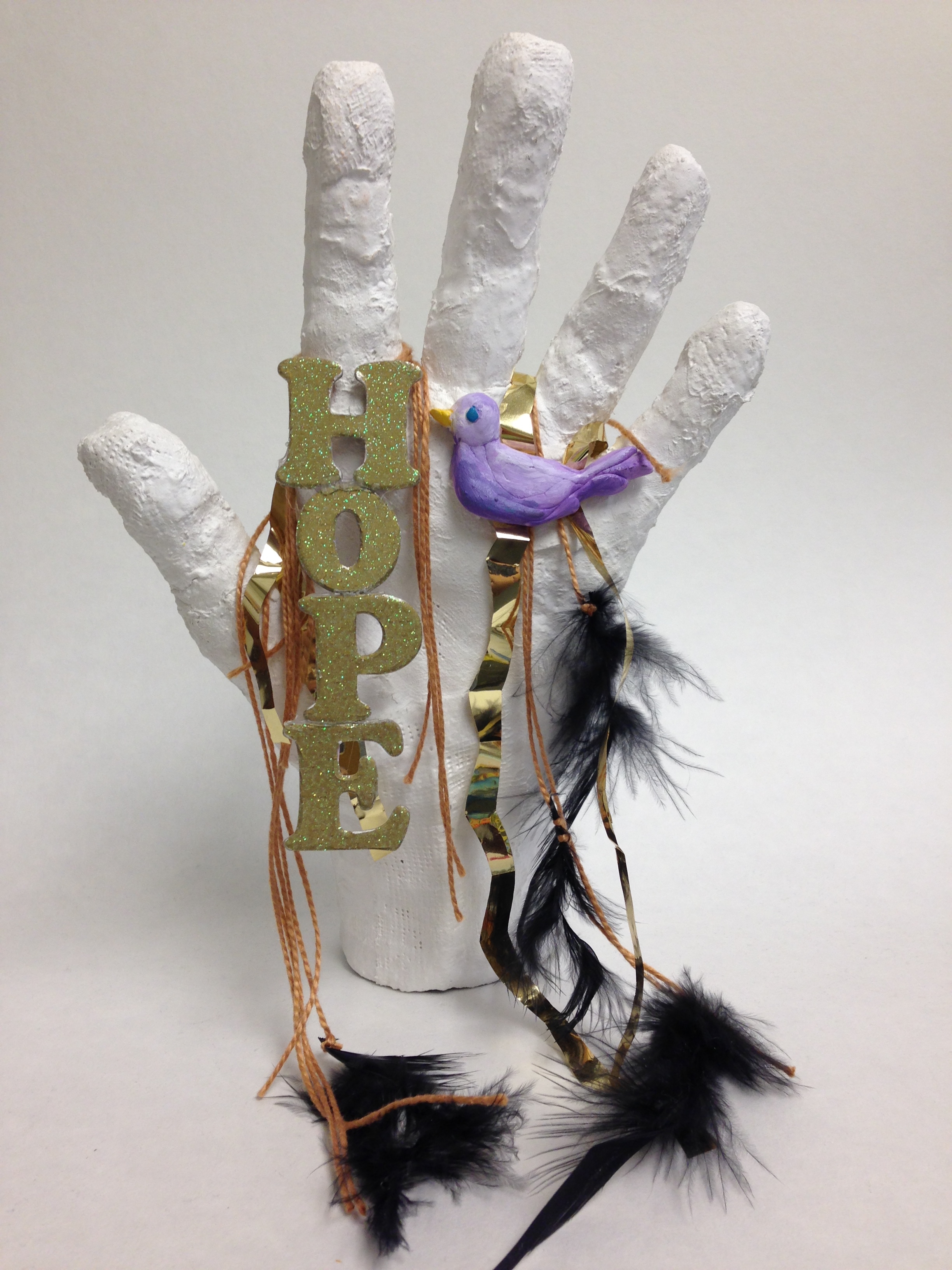 Plaster cast of a hand holding a purple bird, black feathers and the word "HOPE."