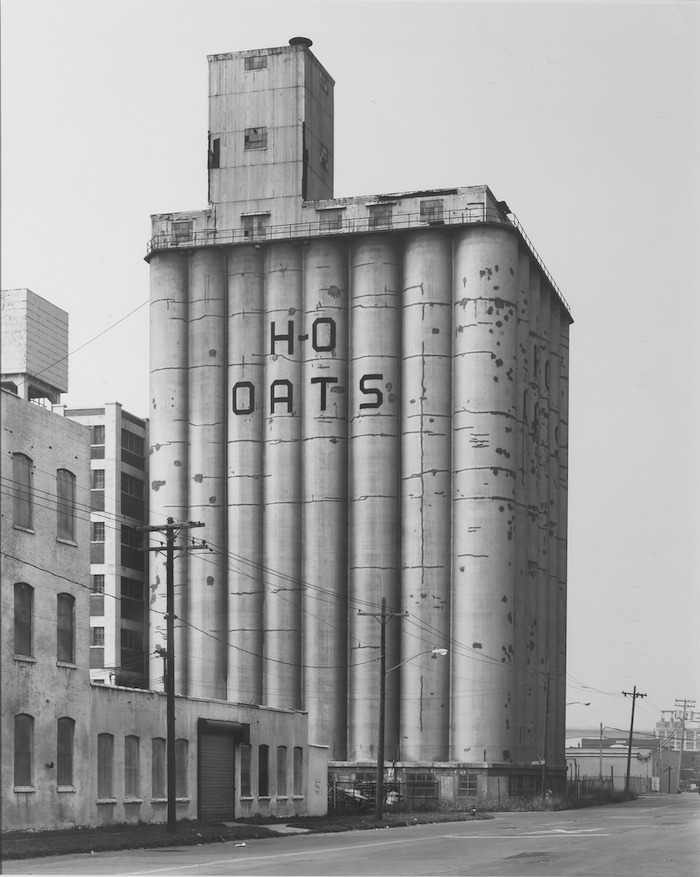Black and white film photo of a large grain elevators with the words "H-O OATS" printed on the side