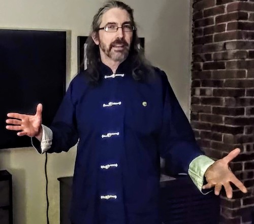 A man with long hair and glasses wearing a blue Tai Chi robe 