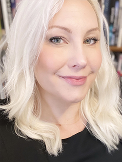 A headshot of a white woman with platinum blonde hair wearing a black shirt