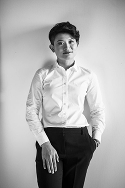 A black and white photograph of an Asian American woman with short dark hair wearing a white dress shirt and black pants