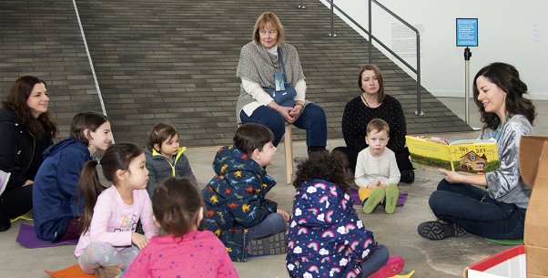 A woman reading a book to a group of children sitting on the floor in front of her