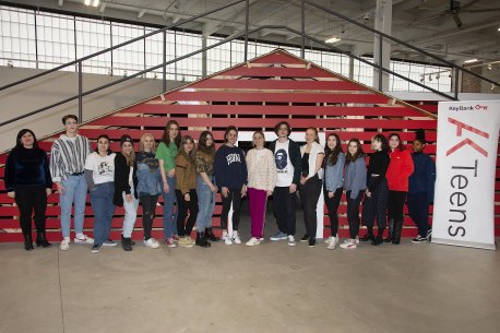 A group of teens standing in front of a roof built in the middle of a large industrial building
