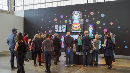 People gathered around an artwork composed of several screens mounted to a black wall
