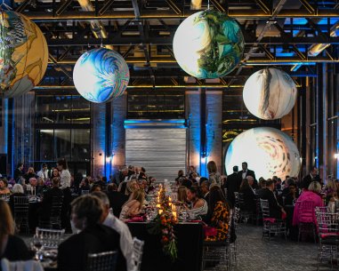 People seated at large, decorated tables while large sphere-shaped artworks hang overhead