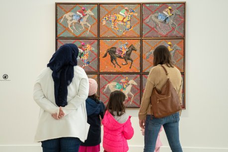 Two women and three kids looking at an artwork showing nine panels with a jockey on a horse in various colors