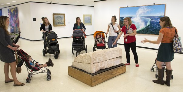 Parents with children in strollers look at art