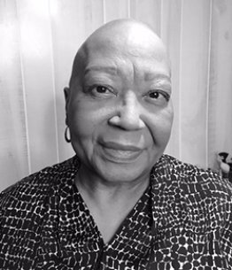 Black and white photo of a Black woman with a bald head and a patterned shirt
