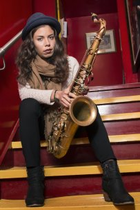 Melissa Aldana sitting on stairs holding her saxophone
