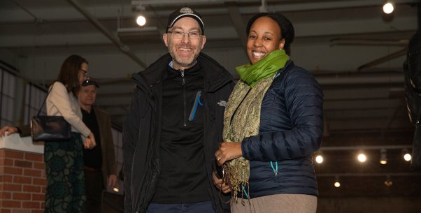 A white man and an African American woman standing on a rooftop smiling at the camera