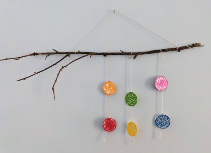 A tree branch with colored circles hanging off of strings attached to it