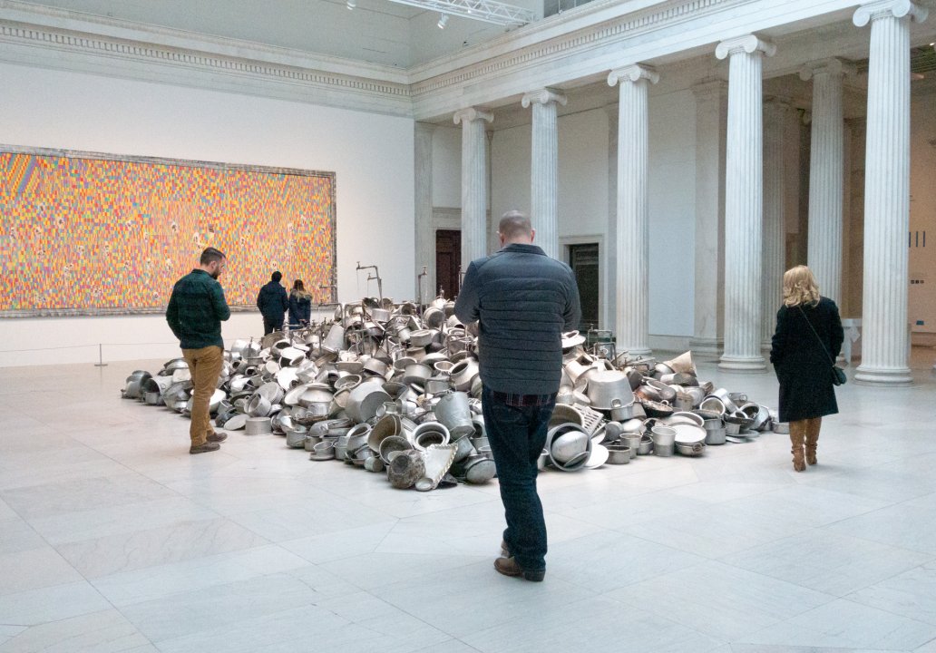 Guests around Subodh Gupta&#039;s This is not a fountain, 2011–13, in We the People: New Art from the Collection. Pascale Marthine Tayou&#039;s Chalk Fresco A, 2015, is in the background.