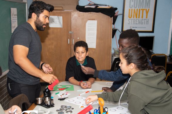 A Latinx man leads three kids in a button making activity