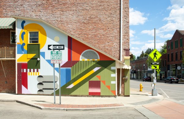 A colorful mural with geometric shapes and colored backgrounds on the side of a building on a street corner
