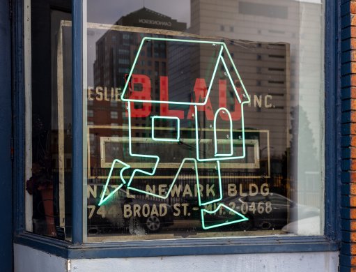 Green neon sign in the shape of a house with legs running displayed in a storefront window