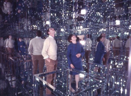 A man and a woman in a mirrored room looking up at their reflections in the ceiling