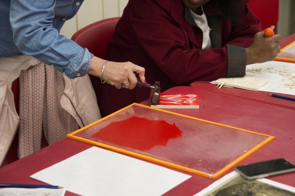 A hand rolling red paint onto a screen printing block on a table with a red tablecloth