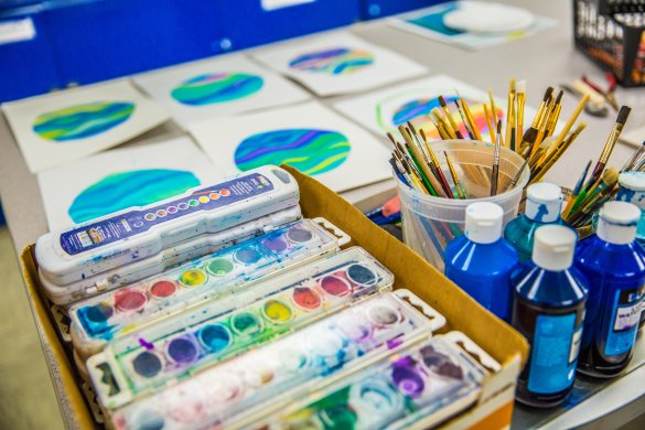 Watercolor paint sets, paintbrushes, and small circular watercolor paintings on paper laid out on a table