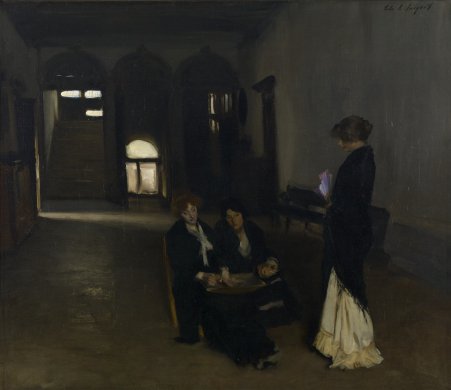 A standing woman approaches two seated women stringing beads over a shallow wooden bowl in the center right of this painting, which is set in a large, mostly empty room. An open doorway and windows at the back of the room provide limited light. At right, a bench is positioned against a wall. The two seated women wear dark dresses while their standing companion wears a white dress mostly covered with a dark shawl.