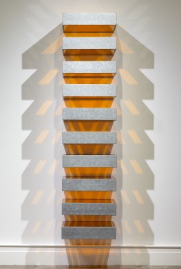 Ten identical boxes industrially fabricated out of galvanized iron and orange Plexiglas protrude seemingly weightlessly from the wall in a vertical stack. Each box is separated from the unit above and below by a space equal to its height. When lit from above, the sculpture casts a dramatic pattern of orange and gray shadows on the adjacent walls and floor.