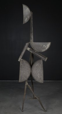 A series of three-dimensional geometric forms balance on two forked legs in the front and a third leg in the back. Overall, the sculpture abstractly mimics the human form: a vertical half circle at the top serves as a head and is connected to the rest of the work by a long vertical rectangle that resembles a neck. Two additional long rectangles at the center of the work sit alongside further half circles that resemble a shoulder and two hips.