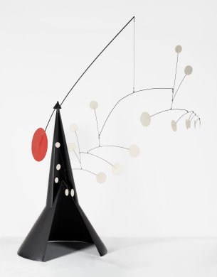 A large playful sculpture made of thin sheets of black metal forming a partially open cone that stands on its circular base. A thin metal rod is balanced across the cone’s pointed top. Numerous interconnected wires and rods, each of which ends in a small white metal circle, hang from one side of the rod. The weight of the many wires and circles on one side of the central rod is counterbalanced and held in equilibrium by a single red circle on the rod’s other end.