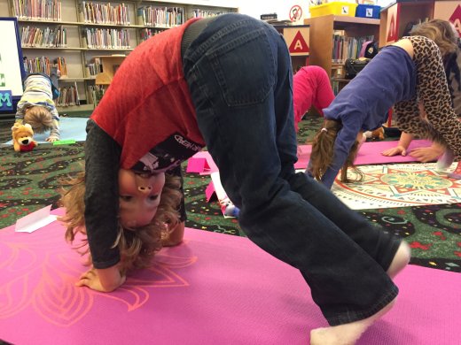 A kid doing the yoga pose downward dog on a pink yoga mat