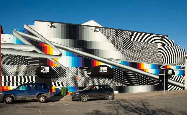 A large mural on the side of a building with sections of bold color and sections of black and white stripes