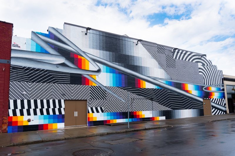 Large mural on a brick building featuring geometric shapes and patterns that have blocks of rainbow colors and black and white.