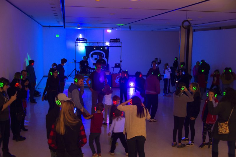 A dark room with a crowd of people with different light up headphones and a DJ (for a silent disco) 