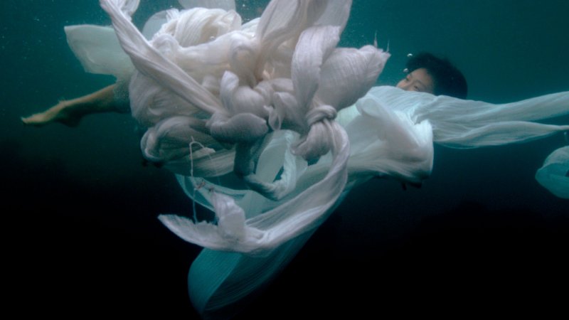 Film still of a person underwater wrapped in white fabric 