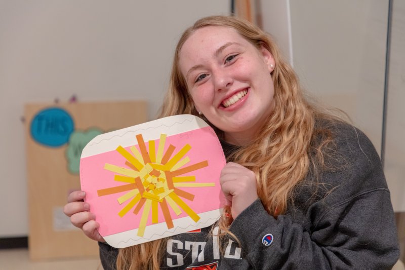 A young woman holding up a collage sun and smiling