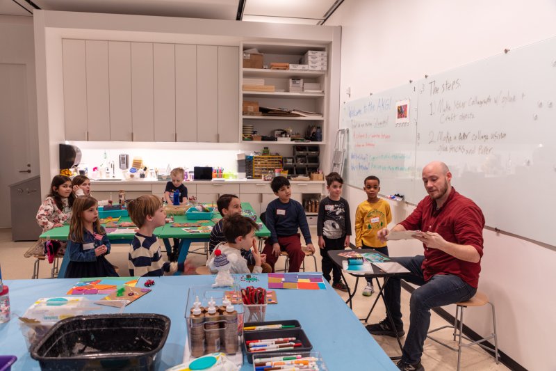 A group of young children in an art studio looking to a man leading the class