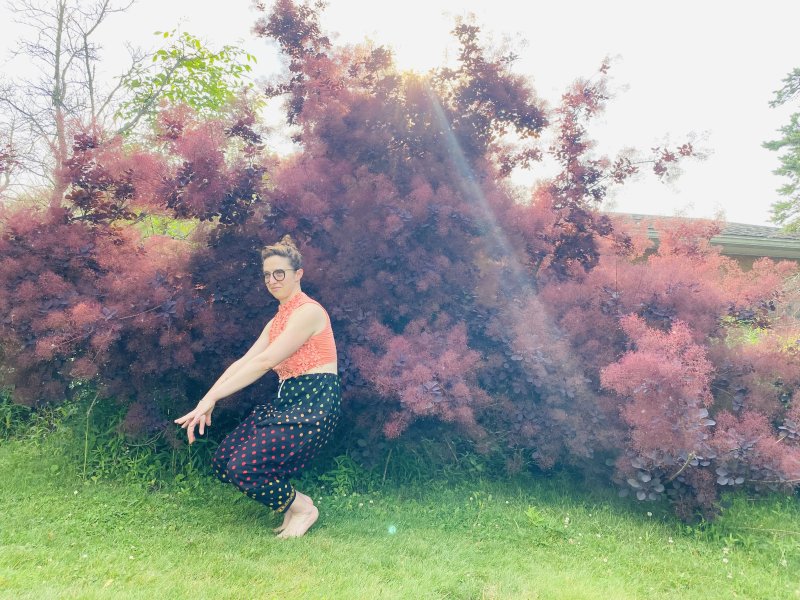 A woman crouching in front of a bush 