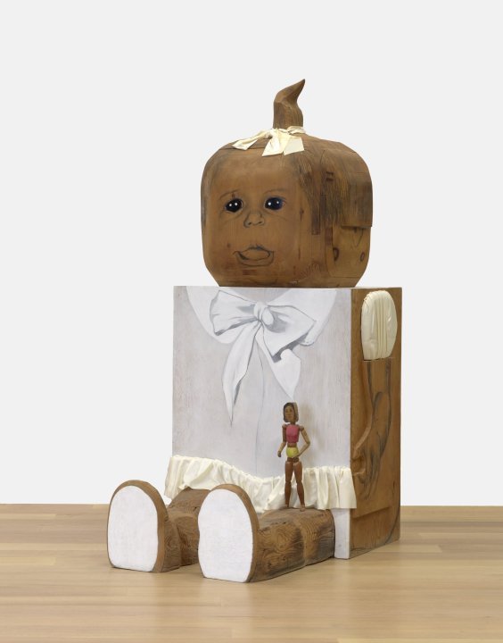 A large wooden sculpture of a baby girl with a small figure on her lap