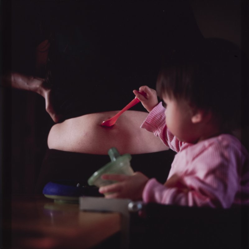 Photo of a woman's pregnant stomach and her young daughter holding a spoon up to it