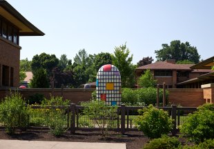 A large colorful ceramic sculpture on a green lawn behind a fence
