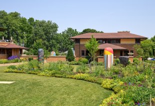 Three large ceramic sculptures on a green lawn in front of two brown brick buildings