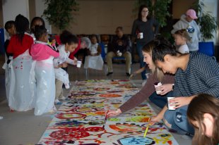 Adults and children paint on a large roll of white paper on the floor