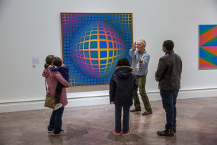 Two families on a tour in front of Victor Vasarely&#039;s Vega-nor, a colorful op art painting